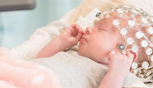 Photo shows a young sleeping infant wearing an array of electrodes on its head. The electrodes record brain activity while the baby sleeps.