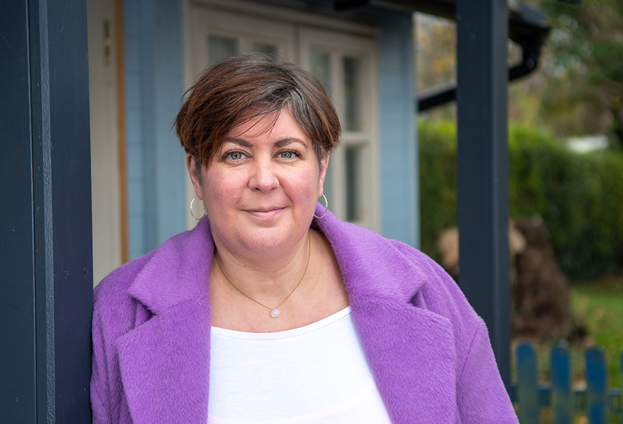 Photograph of a middle-aged woman with short brown hair. She is wearing a white shirt and purple jacket.