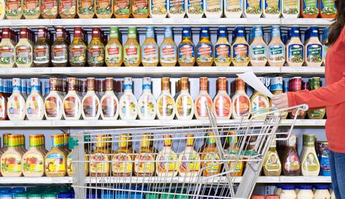 Photo of woman with shopping cart in front of many types of salad dressing on shelves in a supermarket. People are surprisingly loyal to brands. Figuring out the reasons has been challenging for researchers. 