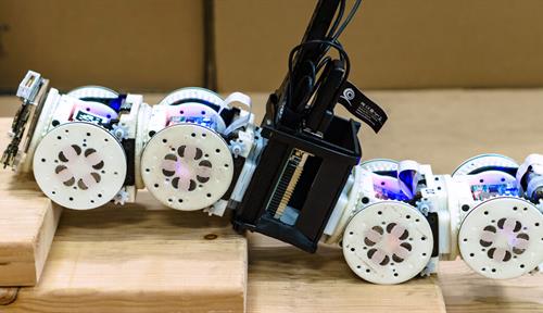 Photo shows four modules of the reconfigurable SMORES-EP robot connected together with a bar in the middle.