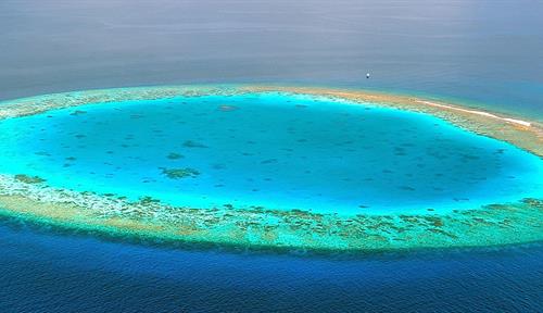 Aerial photo shows a coral atoll in the Maldives. A depression is visible in the middle of the coral ring.