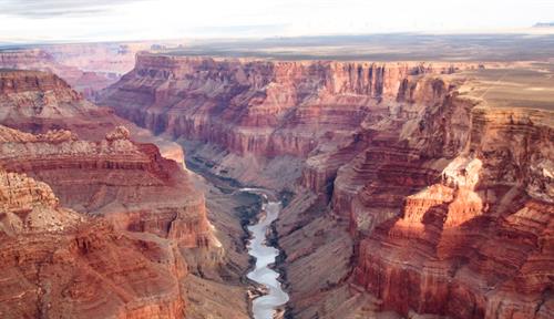 A photo shows an aerial view of a portion of the rim of the Grand Canyon with part of the Colorado River visible. The national park turns 100 this year.