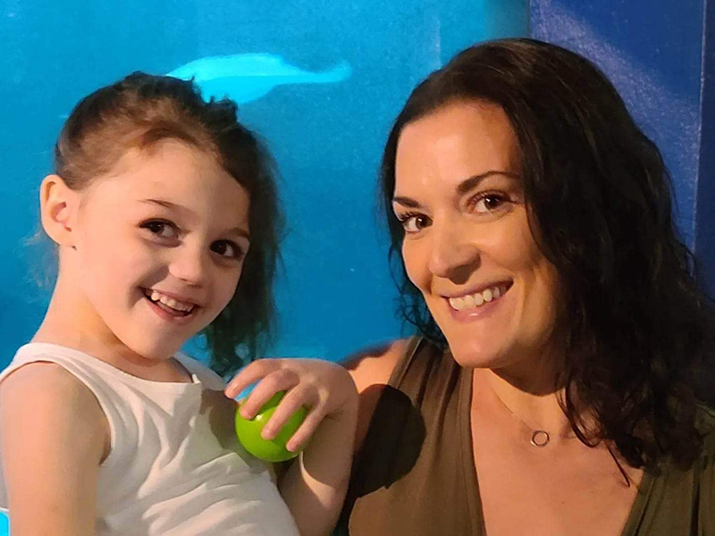 Photograph of a young girl holding a ball and a woman with brown hair. Both are smiling.