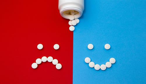 Image shows an open pill bottle. Pills form a frowning face on one side, a happy face on the other side. 