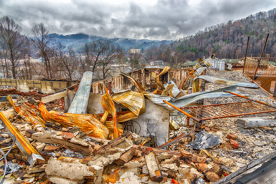 Photograph of a large, burned-out building with charred trees on hills in the background.