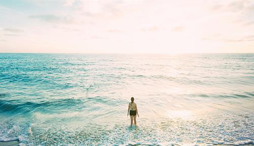 Photograph of a person standing in the waters at the beach, staring out at the ocean.