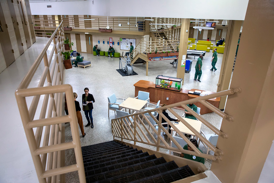 Photo of a prison interior common room with bookshelves, plants and benches.