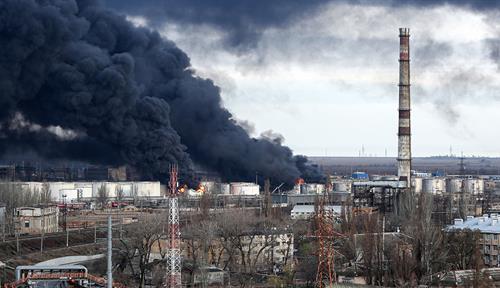  A photograph shows huge clouds of black smoke darkening the sky above the containers and other structures of an oil storage facility. Flames are also visible.