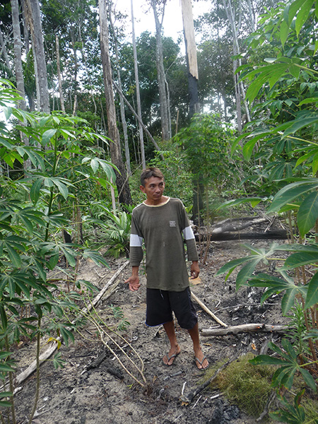 Photograph of a man in shorts and sweatshirt standing among trees.