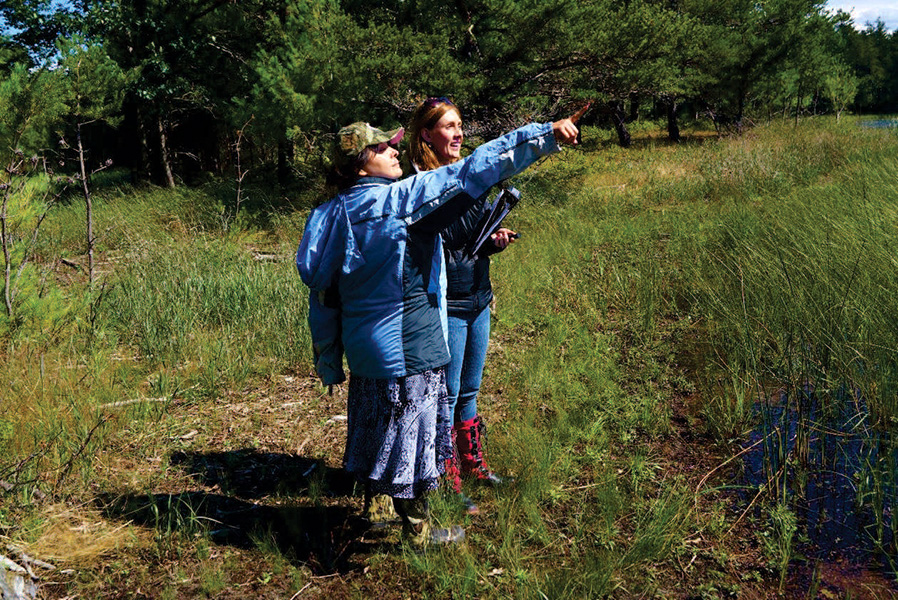 Photograph of a person pointing and another looking on, in a location with lush vegetation.