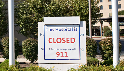 Photo shows the exterior of a large building with a sign saying “This Hospital is CLOSED. If this is an emergency, call 911.”