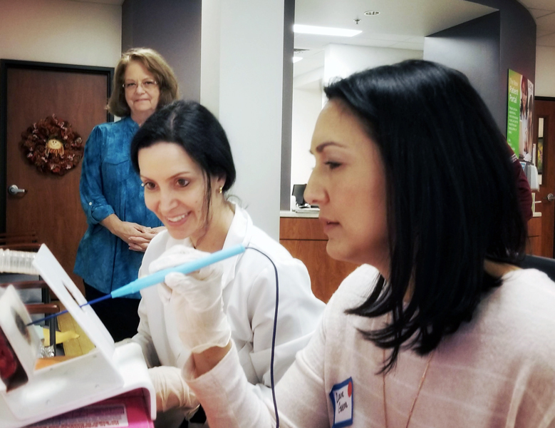 Photograph of two women. One is wielding a surgical instrument in a gloved hand while the other watches.