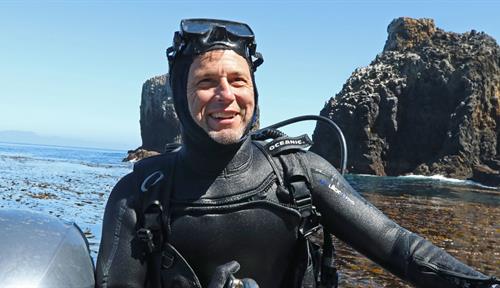 Photograph of Kevin Lafferty climbing onto a small boat from the waters off Anacapa Island near Ventura, California, after spearing fish in March 2018. He’s advising a UC Santa Barbara PhD student on research to determine if reef fish inside protected marine reserves have more or fewer parasites than the depleted fish populations outside the reserve. It’s to test a pattern that has emerged in other studies: that parasites thrive with richness and abundance of marine life.