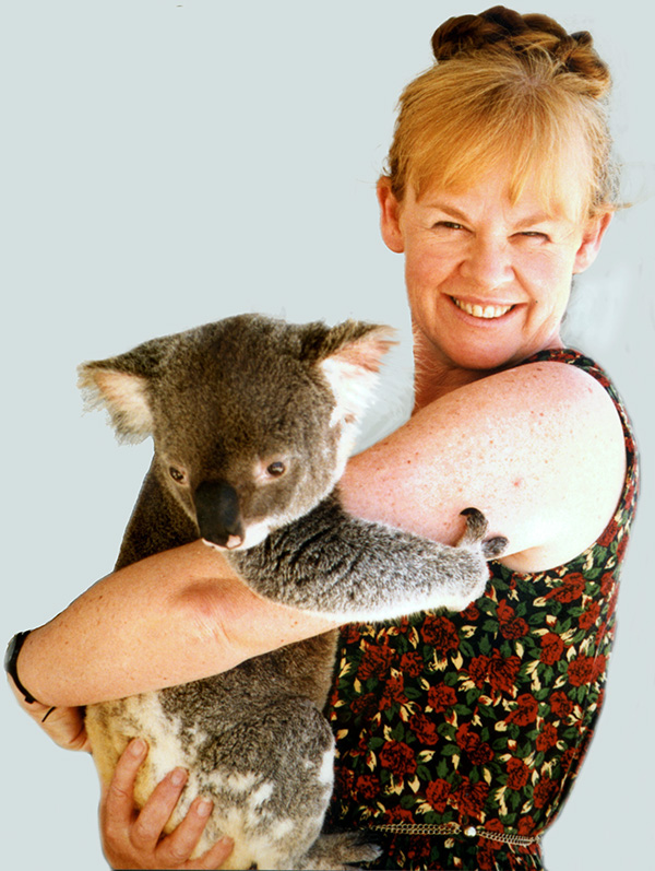 A young woman with red hair in short-sleeved frock is holding a koala and smiling at the camera.